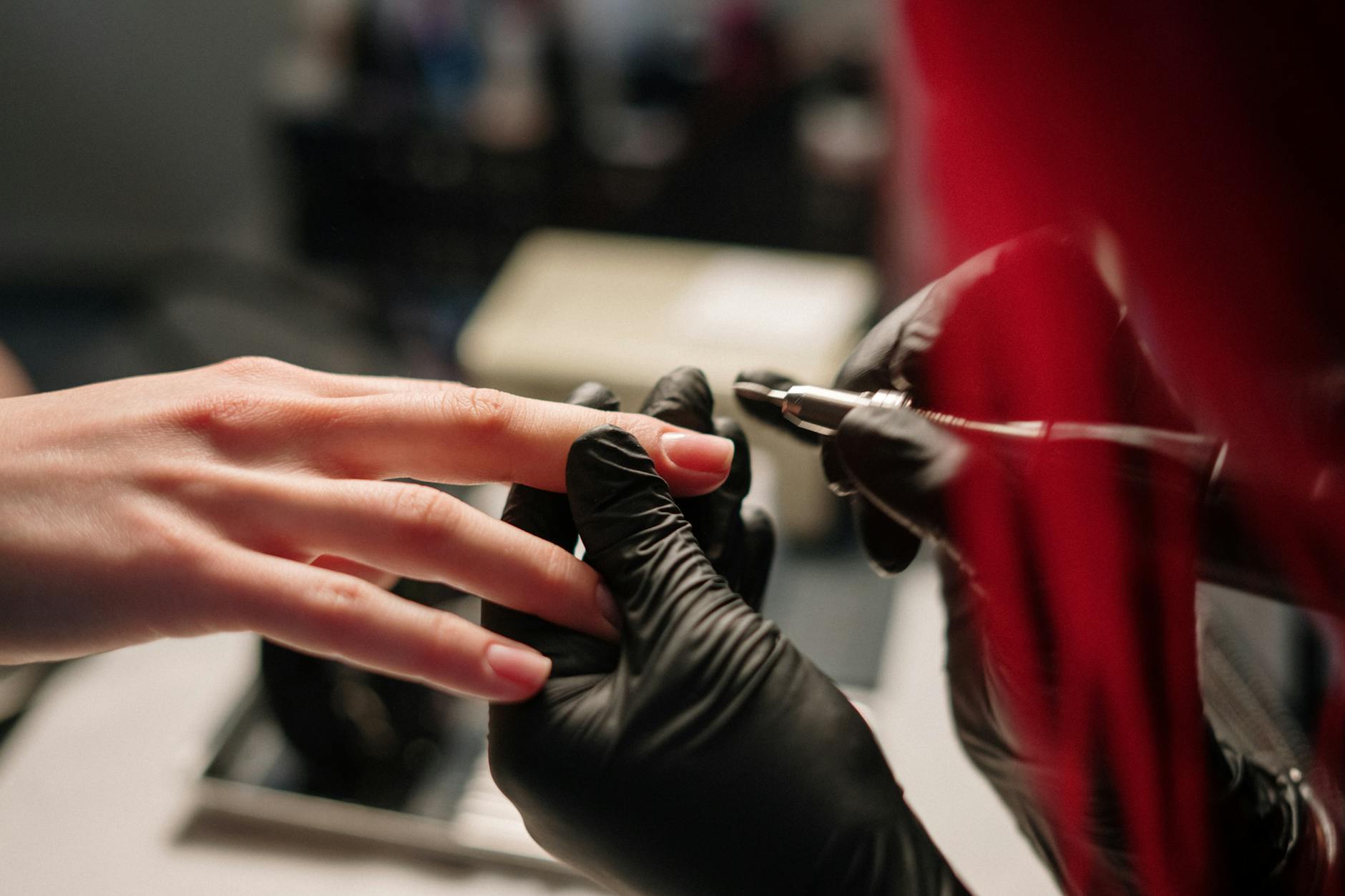 Nail technician using a high speed electric file on acrylic, often a sign of harder MMA acrylic underneath